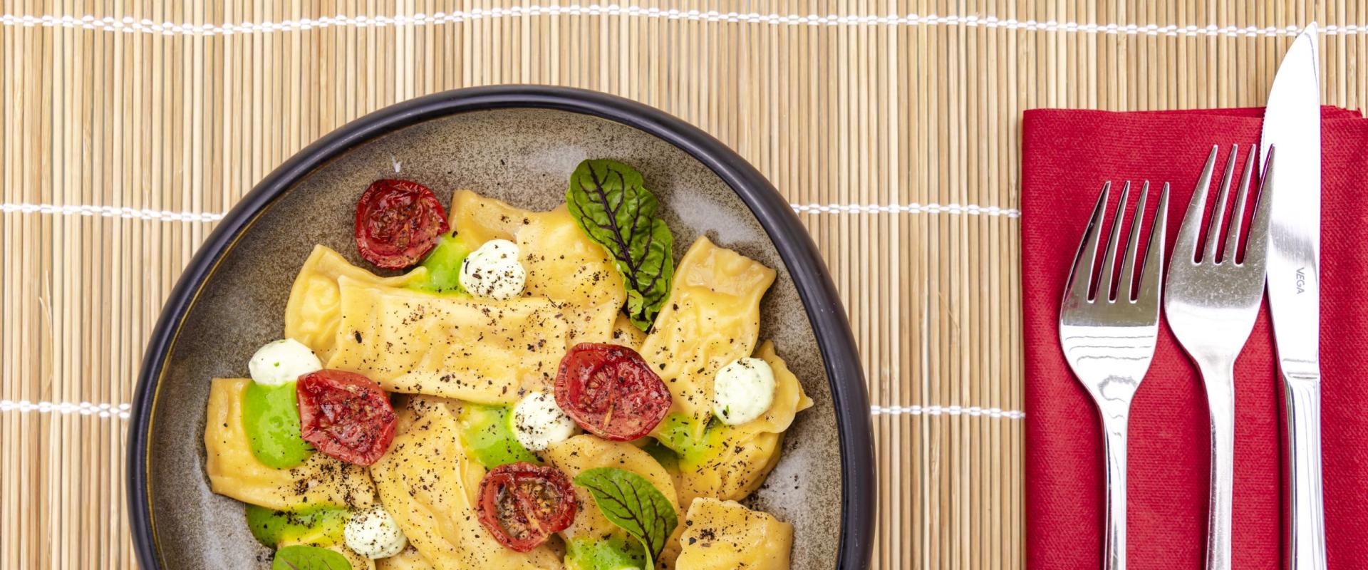 Pasta colorata con pomodori e crema, posate su tovagliolo rosso.