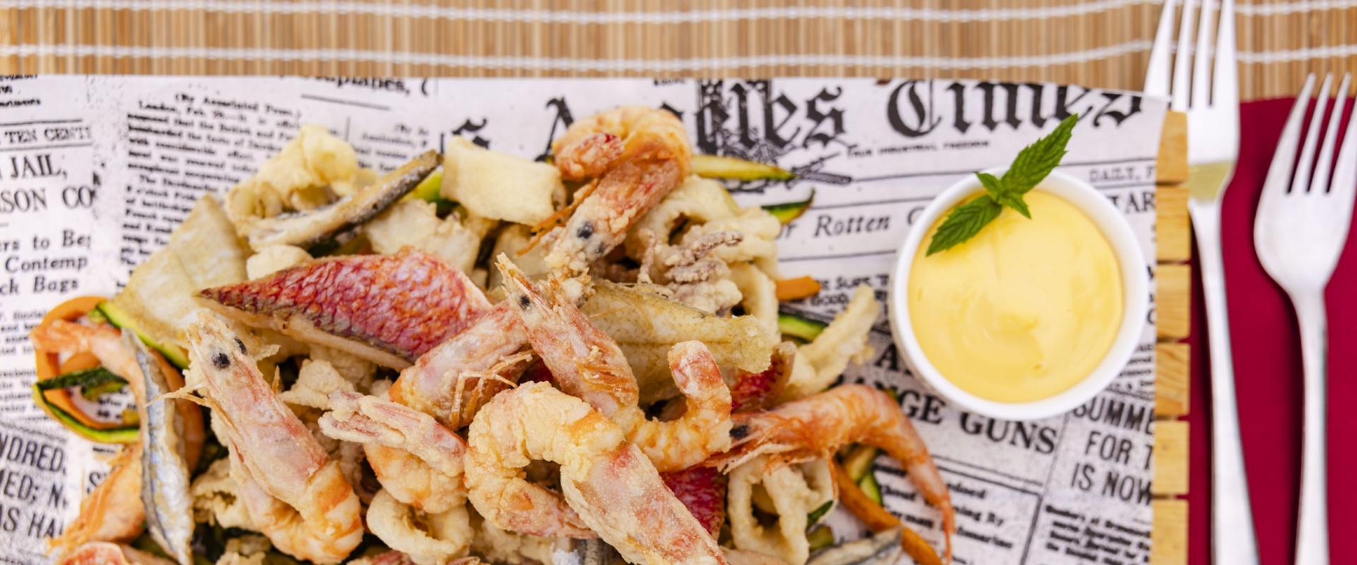 Frittura di pesce croccante con salsa cremosa, servita su carta di giornale.