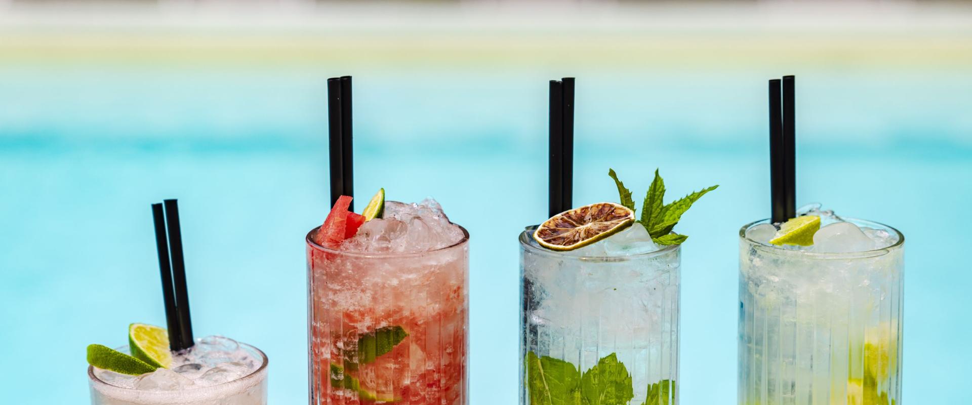 Quattro cocktail colorati e rinfrescanti davanti a una piscina estiva.