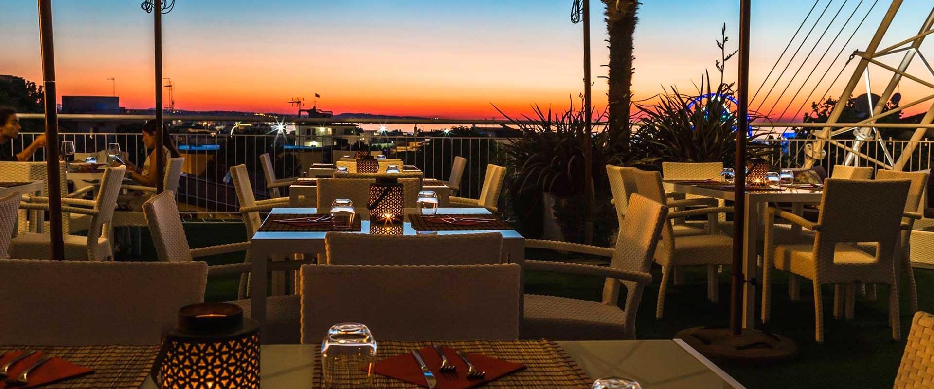 Terrazza al tramonto con tavoli apparecchiati, vista sul mare e atmosfera romantica.