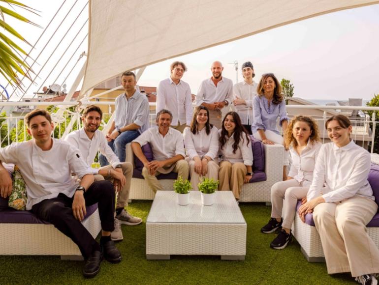 Gruppo di persone sorridenti sedute su divani all'aperto, abbigliamento casual.