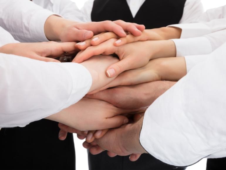 Mani sovrapposte simboleggiano unità e collaborazione in un ambiente professionale.