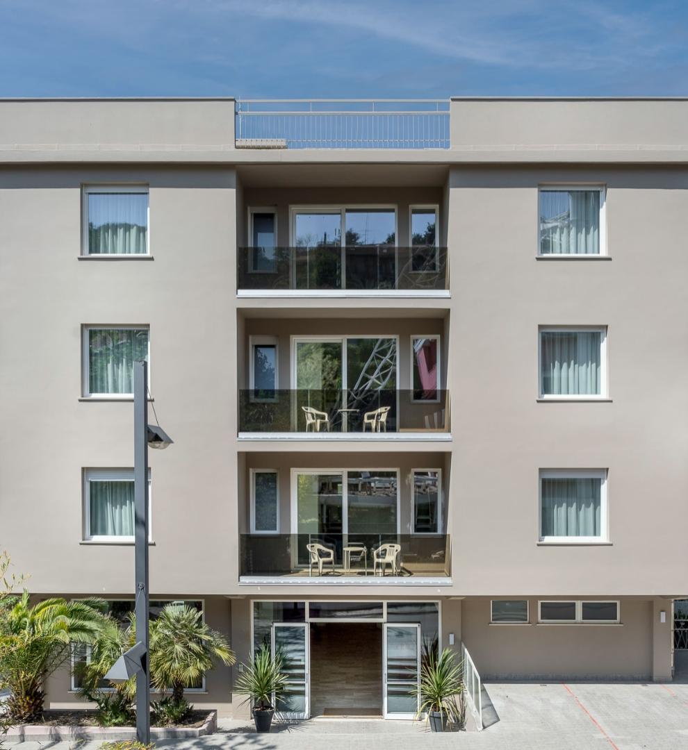 Edificio moderno con balconi, finestre grandi e piante decorative all'ingresso.